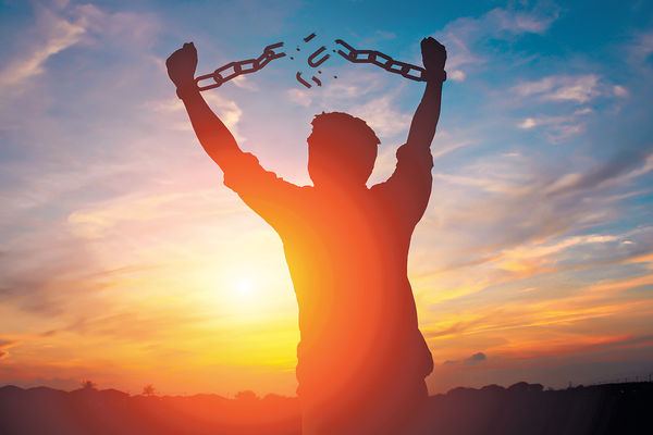 逆光剪影高舉雙手，鎖鏈斷開 · a silhouette raising both arms, the chain breaking