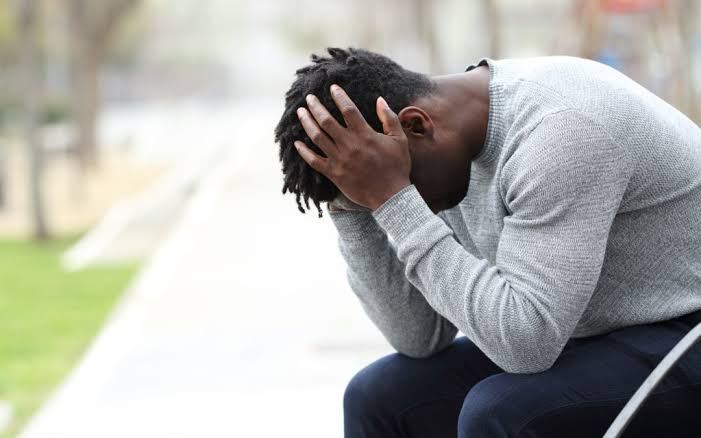 一個人低頭以手掩面坐著 · a man sitting with his head lowered into his hands