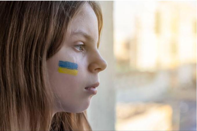 女孩望向窗外的光，臉頰畫著國旗 · a girl looking out through a window toward the light, her country's flag on her cheek